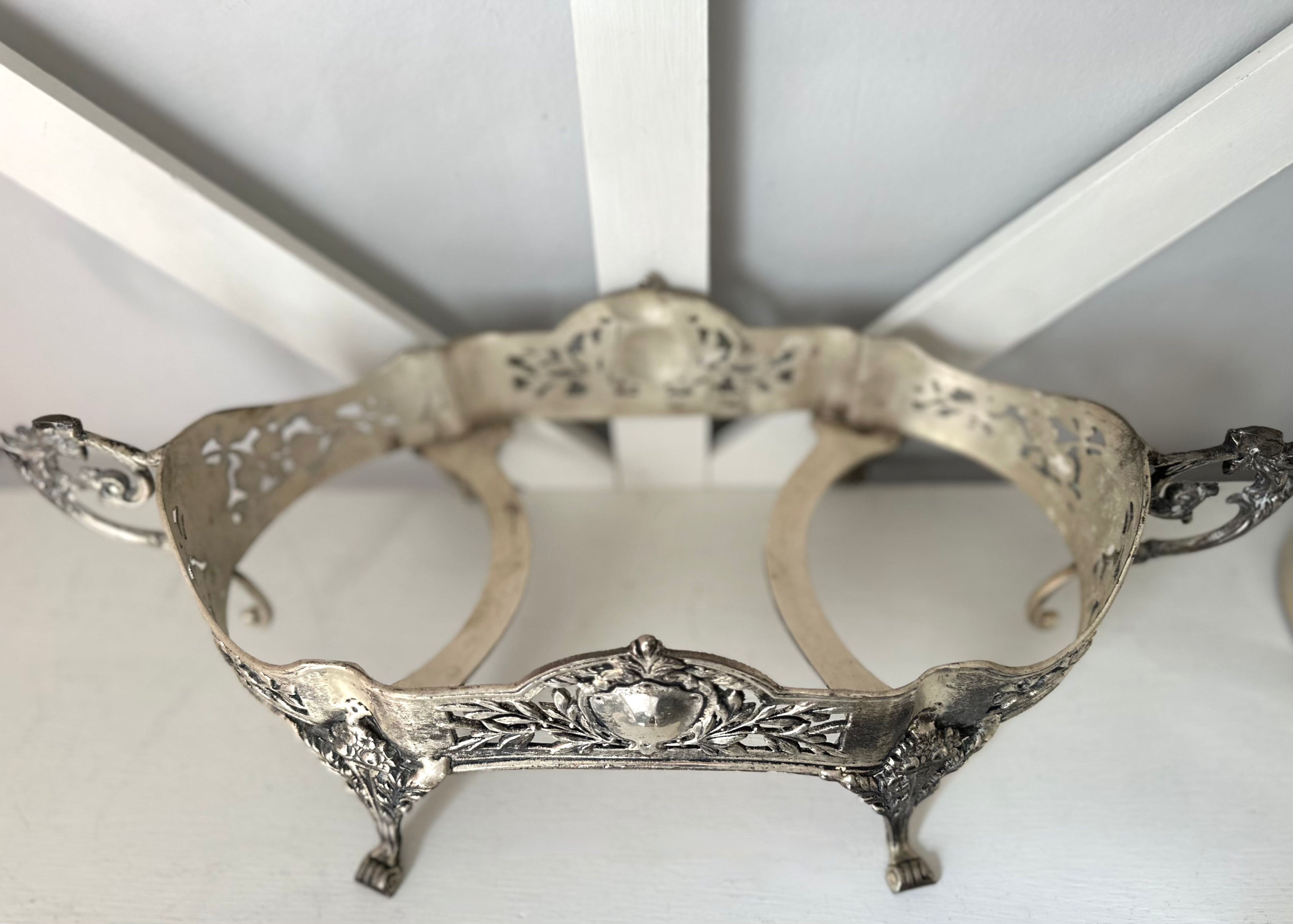 An ornate silver metal stand with decorative filigree cutouts, scrollwork, and small feet, photographed against a white background.