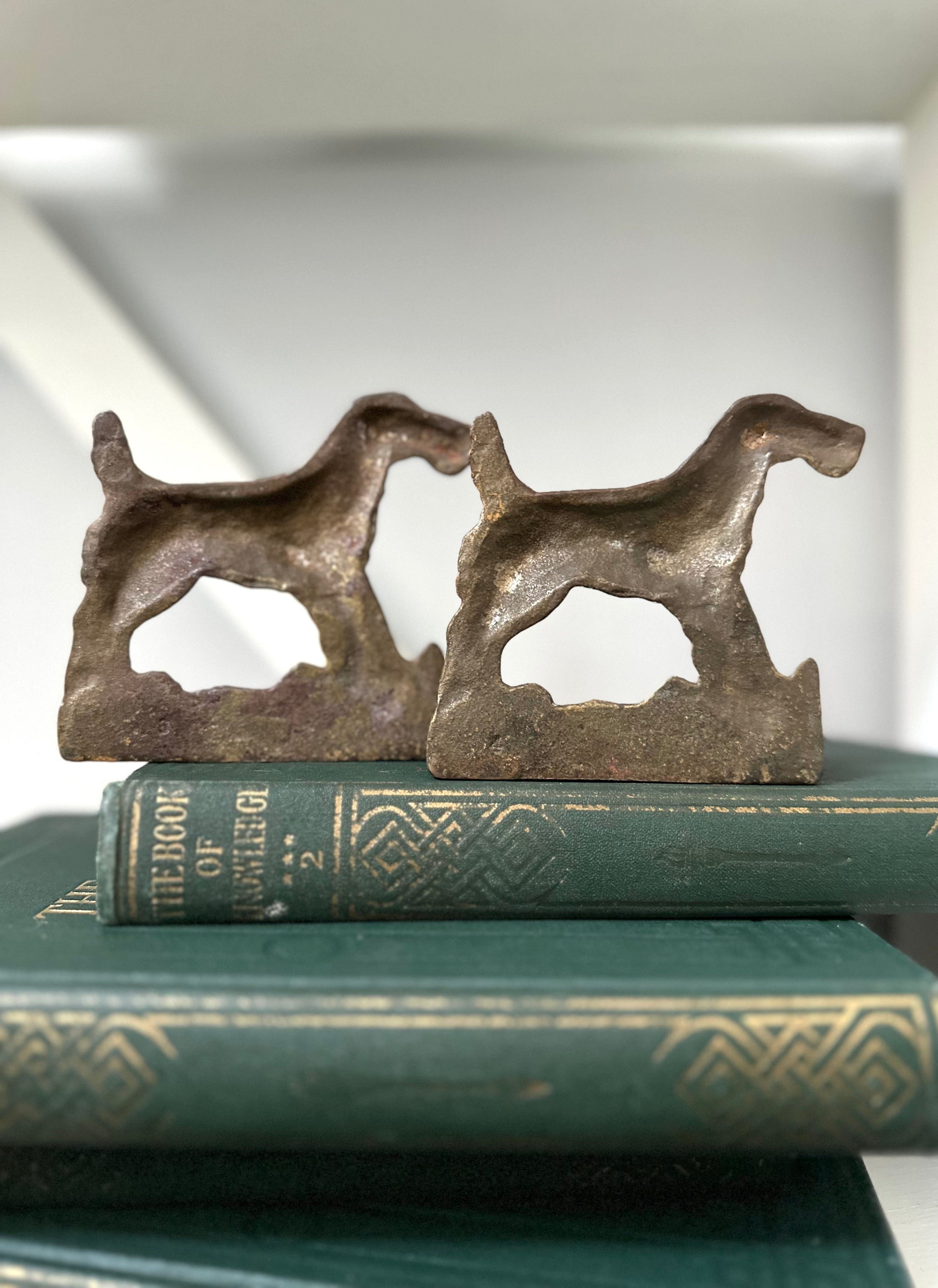 Two metal dog-shaped bookends on top of a green book with gold text.