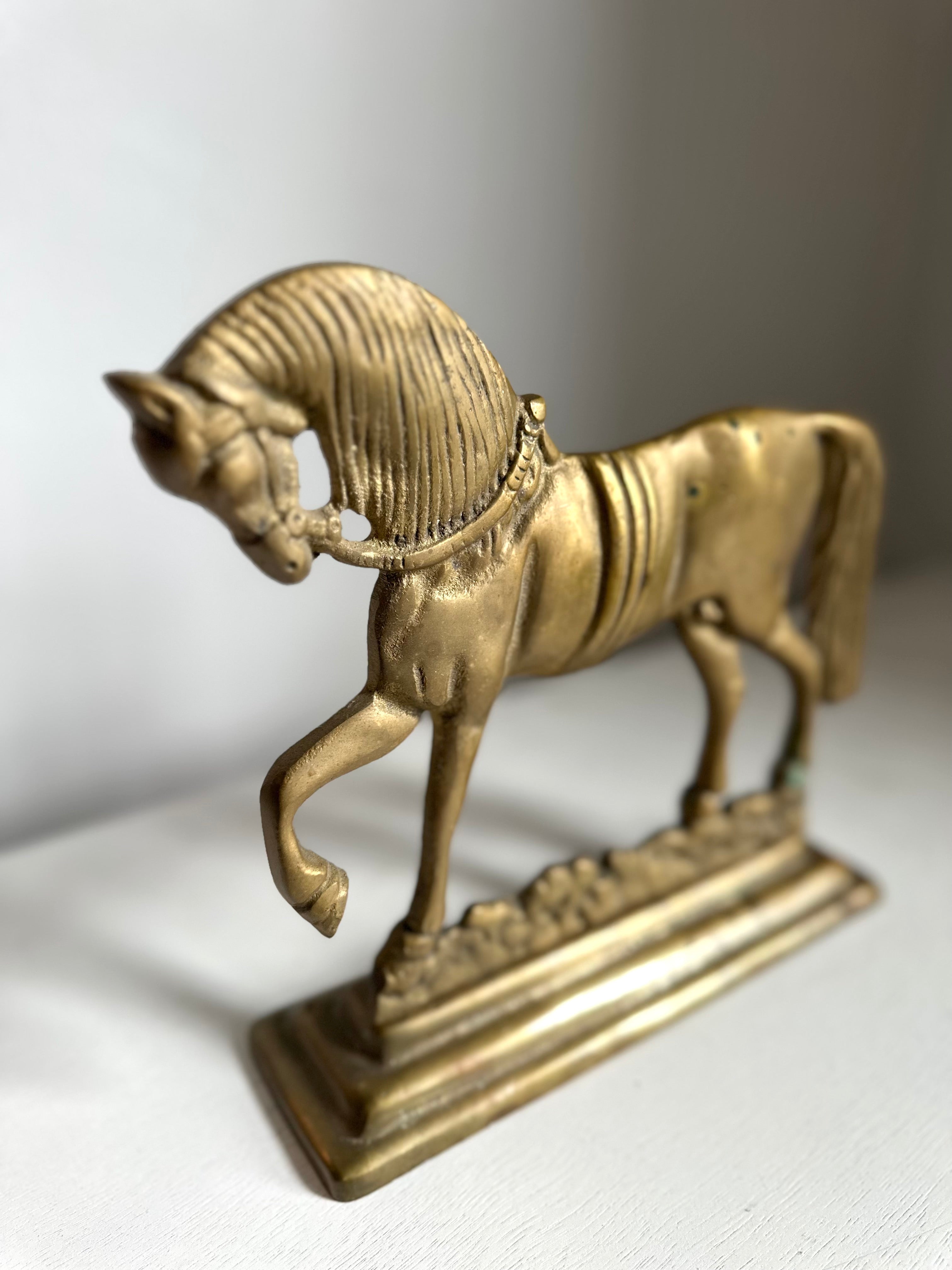 A small metallic horse figurine on a rectangular base, photographed against a plain light gray background.