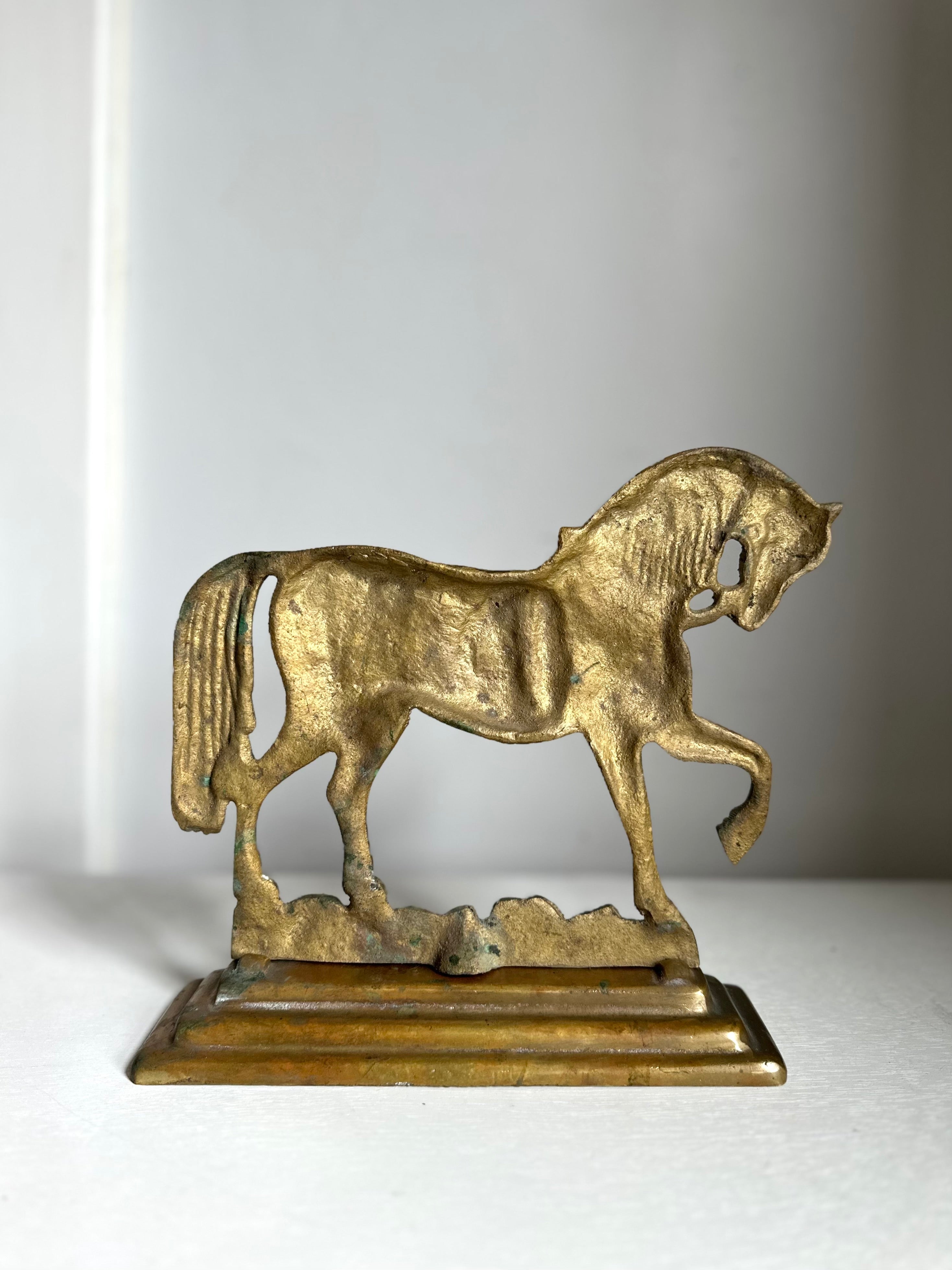 An antique-style metallic horse figurine standing on a rectangular base, photographed against a plain light gray background.