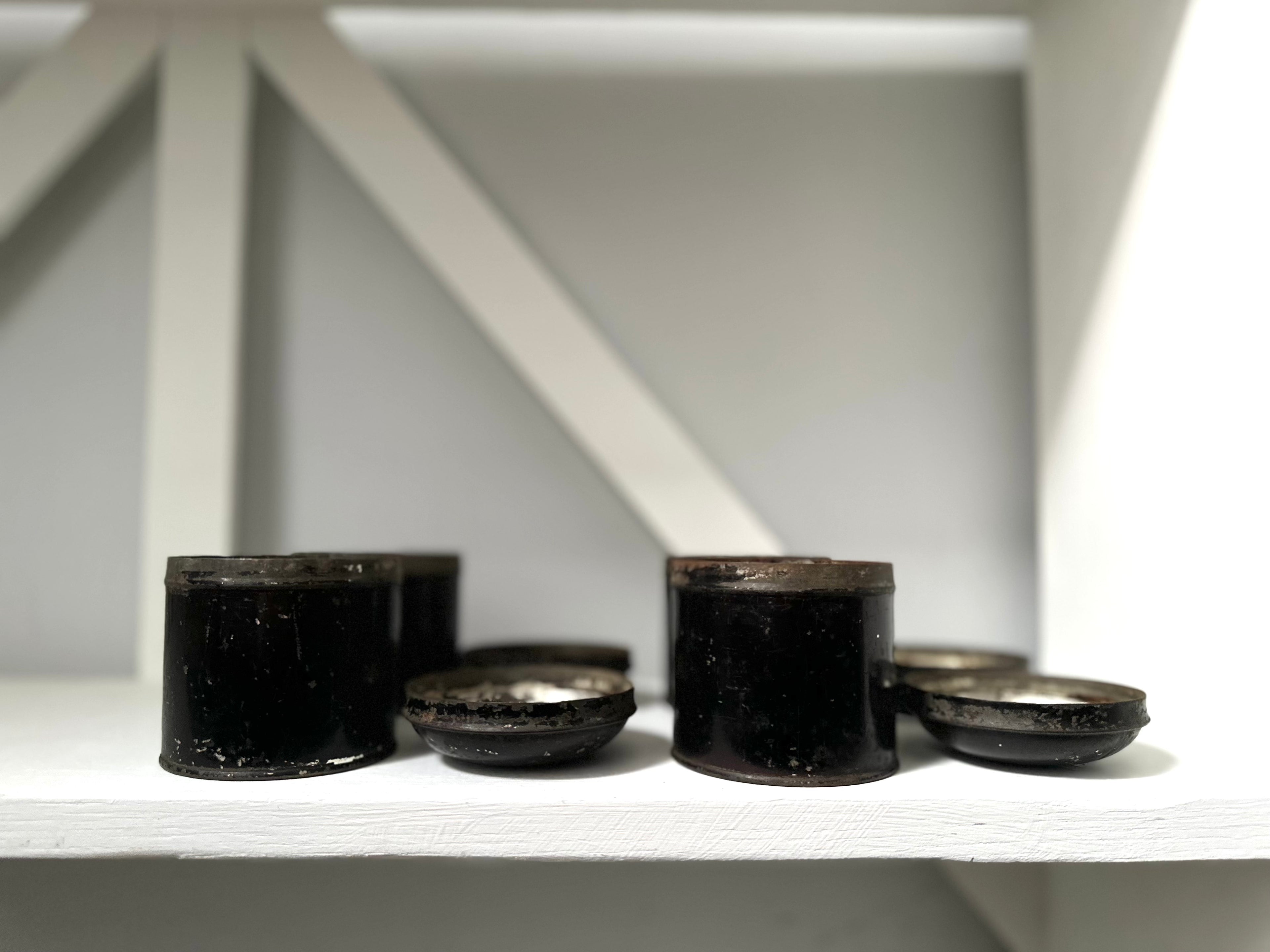 Black cylindrical objects on a white shelf with a white wall background