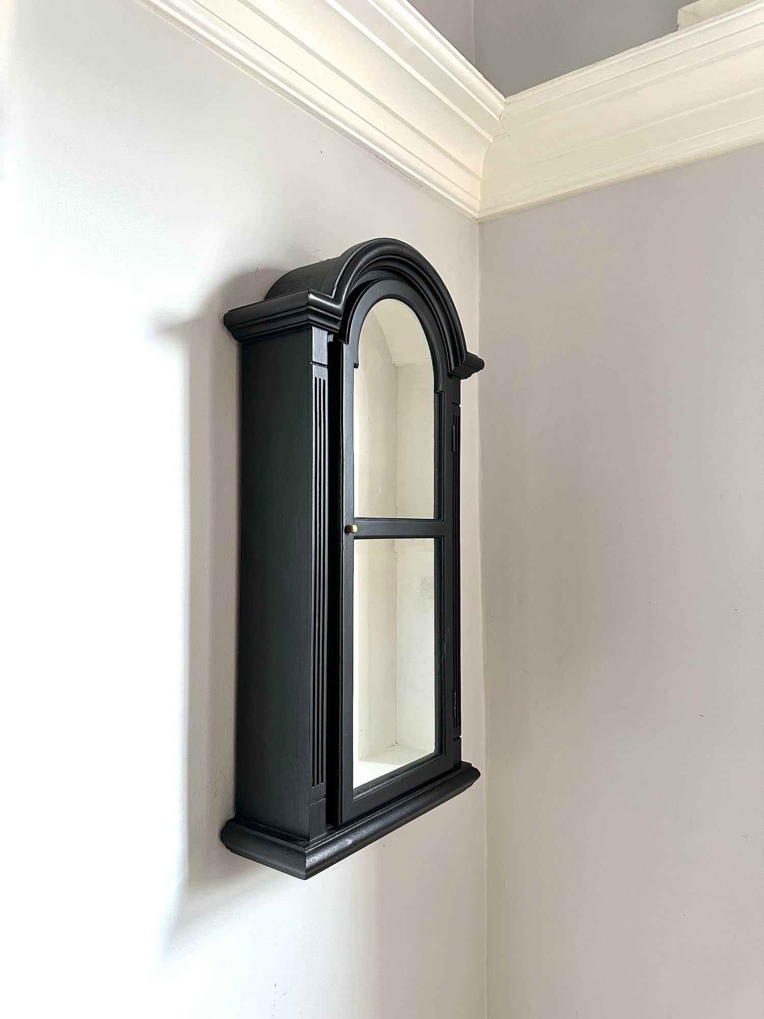Black wall-mounted mirror in a corner of a room with white walls.