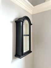 Black wall-mounted mirror in a corner of a room with white walls.