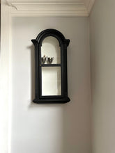 Black wall-mounted display cabinet with glass doors on a white wall.