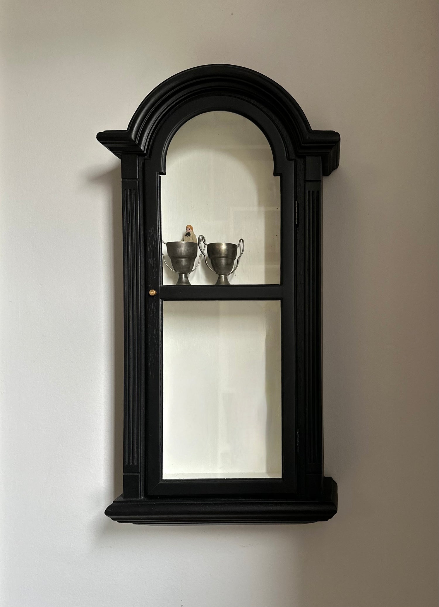 Black wall-mounted mirror with decorative frame on a plain wall