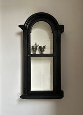Black wall-mounted mirror with decorative frame on a plain wall