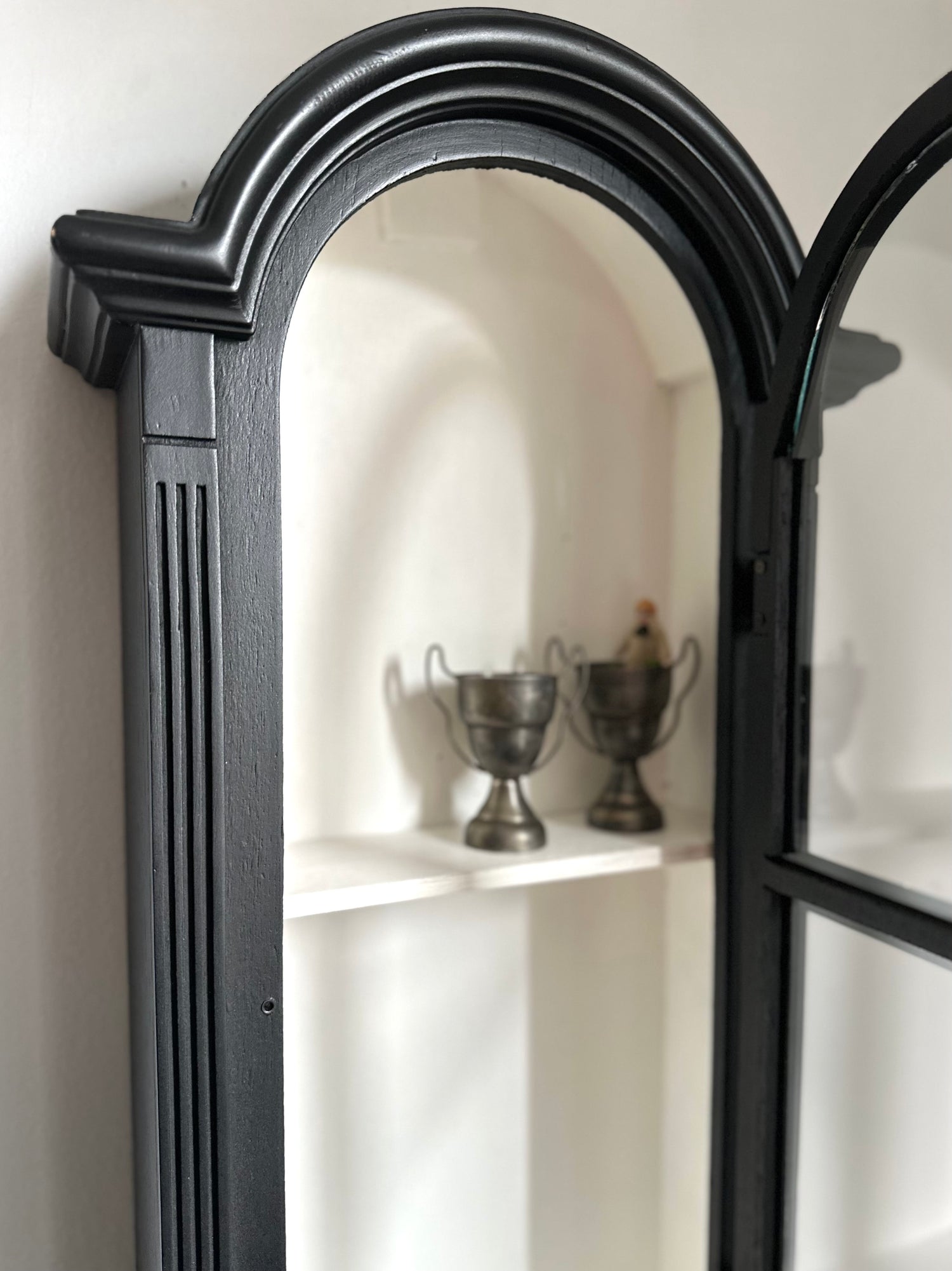 Black-framed curio cabine with decorative arch on a white wall