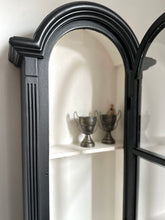 Black-framed curio cabine with decorative arch on a white wall