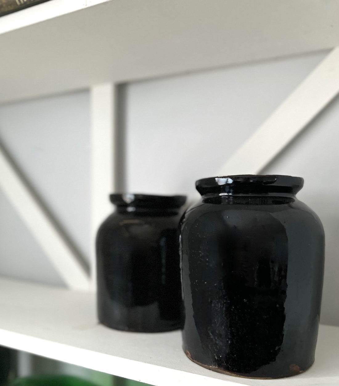 Two black ceramic jars on a white shelf with a neutral background