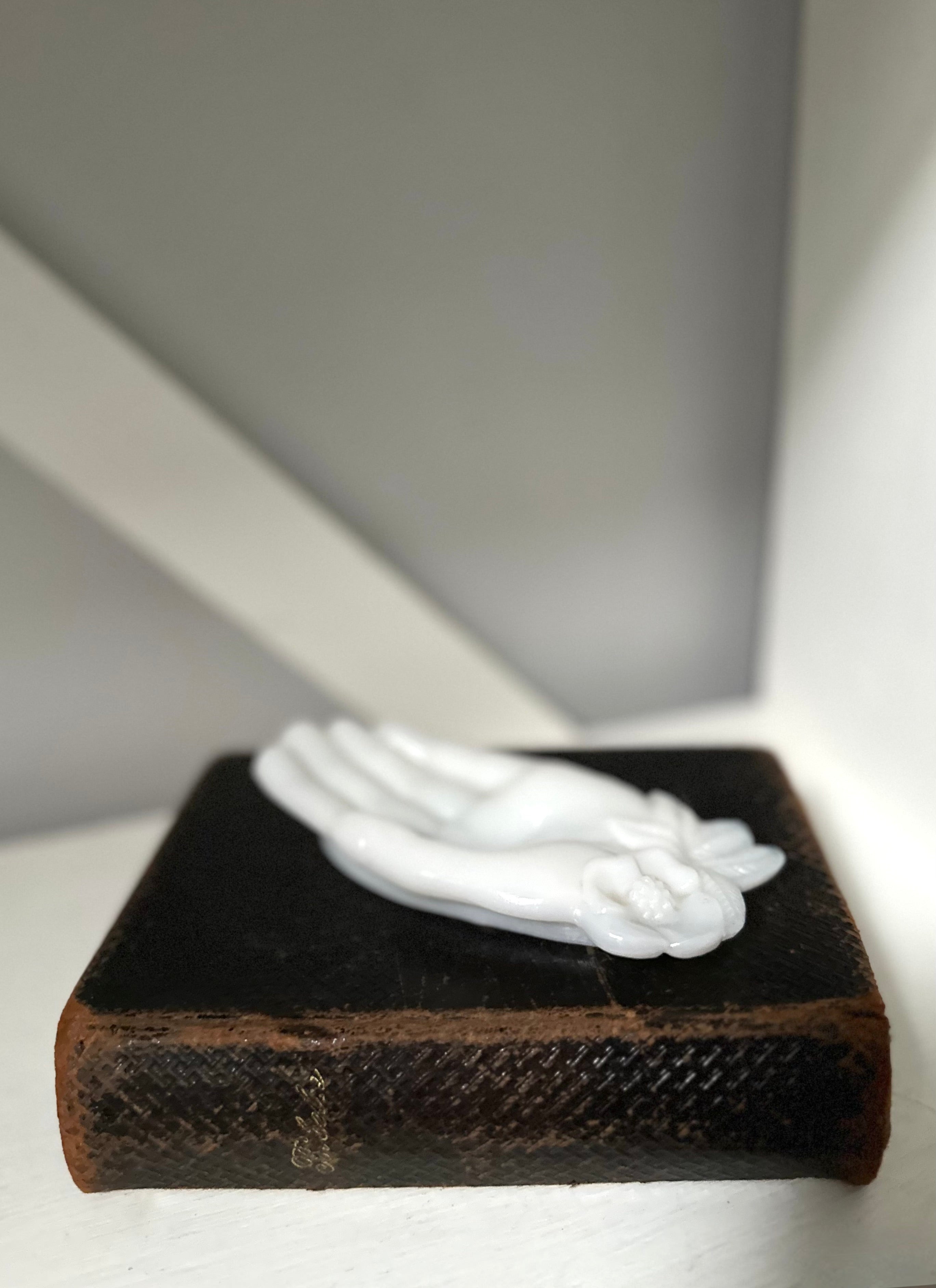 Small white sculpture on a dark brown base against a neutral background