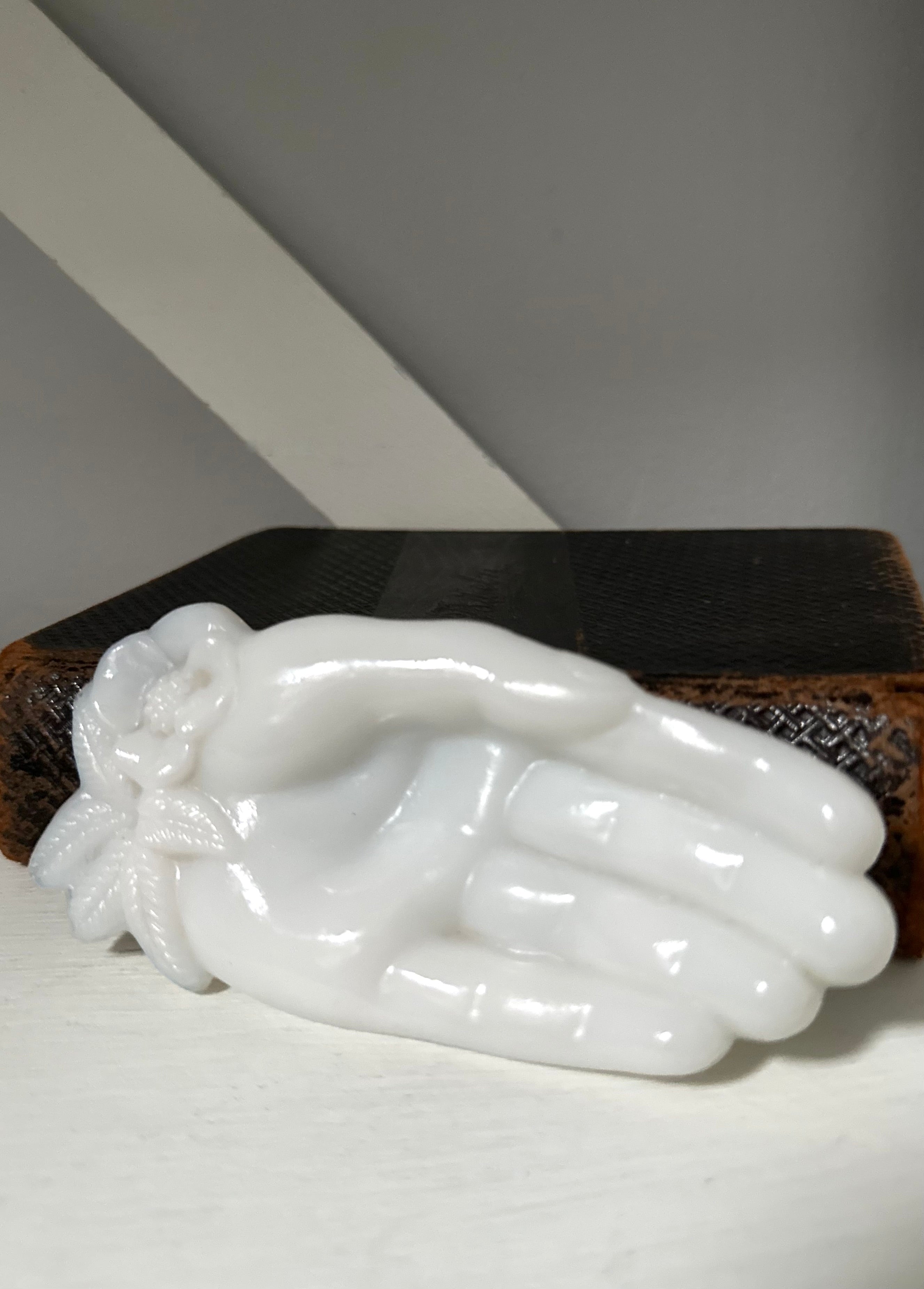 White jade carving of hands on a dark wooden stand against a gray background