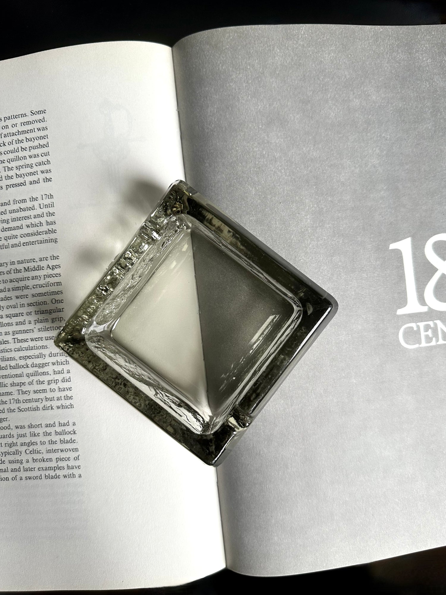 A square transparent green ashtray sitting on an open book