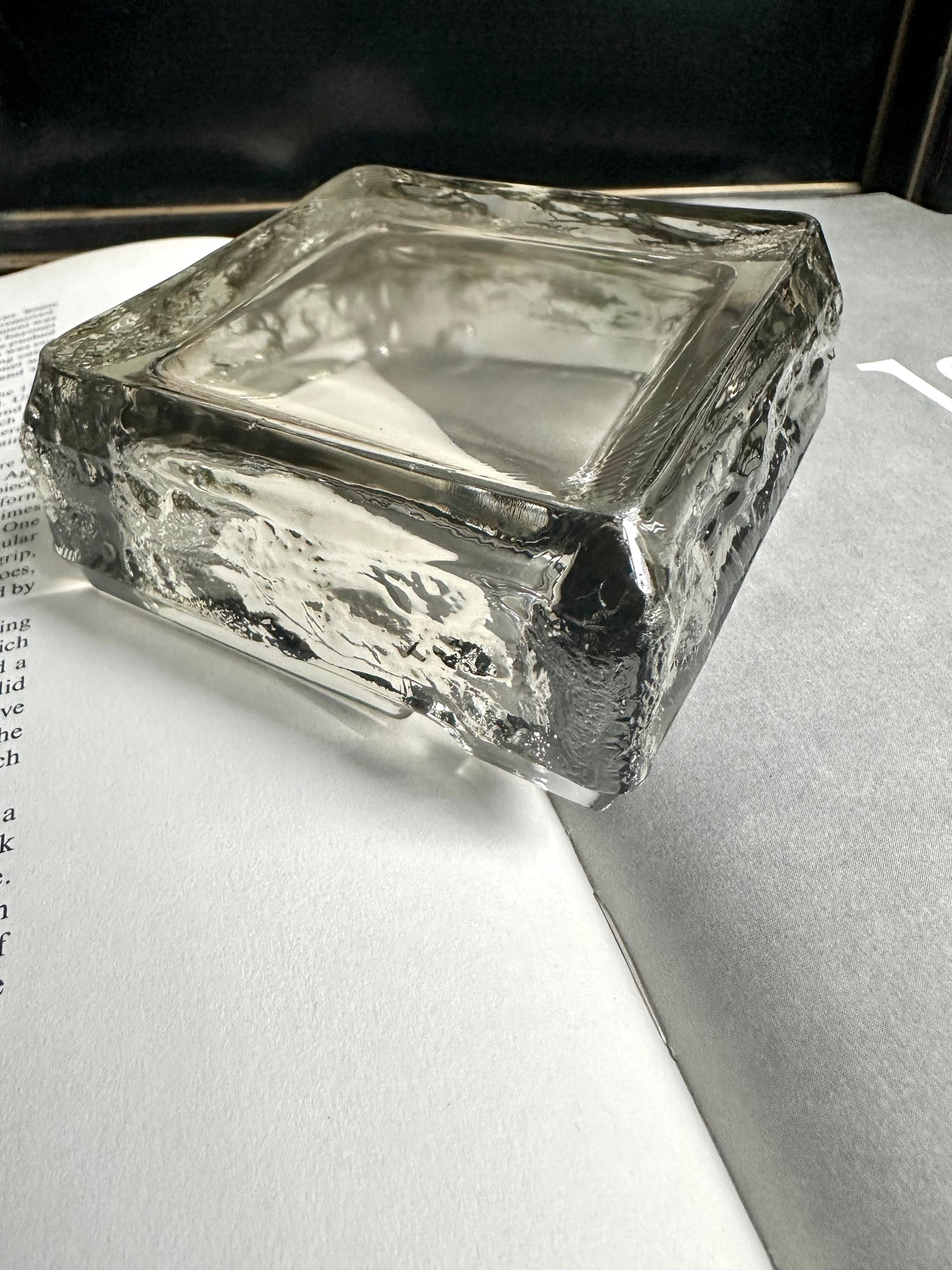 A square transparent green vintage ashtray sitting upside down on an open book