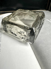 A square transparent green vintage ashtray sitting upside down on an open book