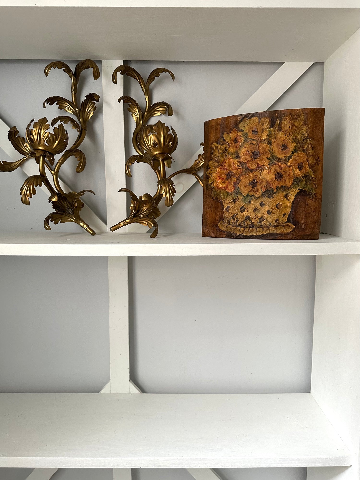 Decorative wall sconces and a floral painting on a white shelf.