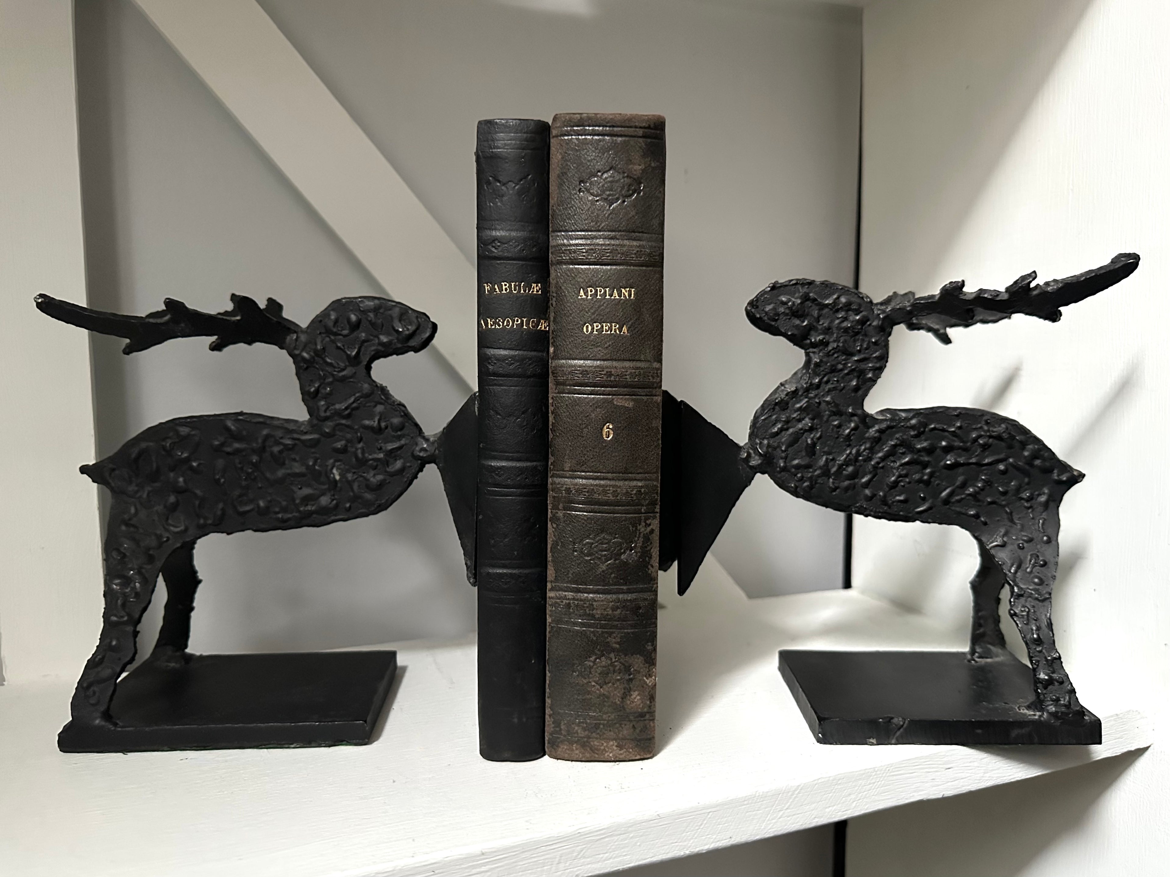 Black cast iron deer bookends holding open a vintage book on a white shelf.