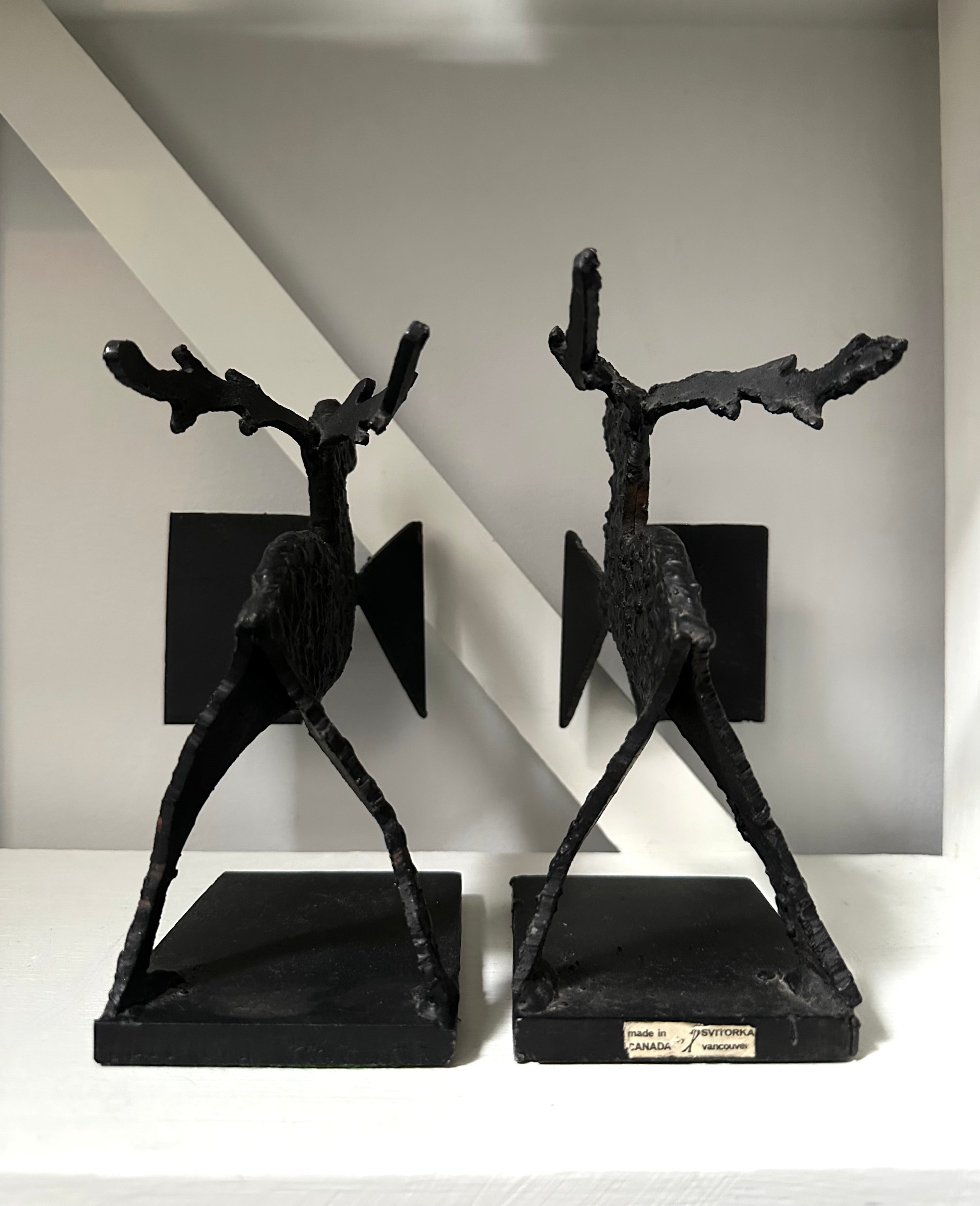 Two black abstract sculptures on a white surface with a gray wall background