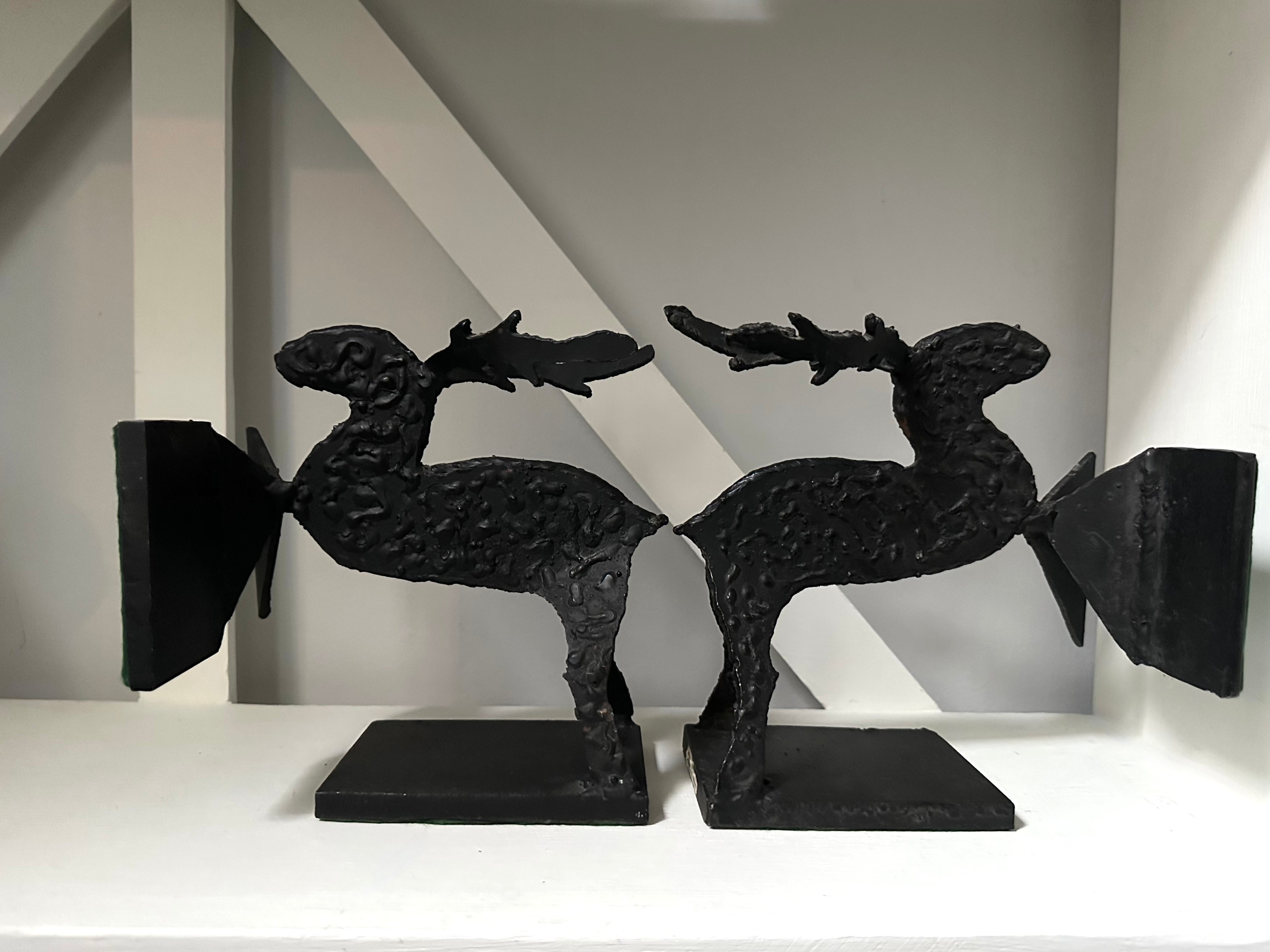 Two black metal moose sculptures on a white surface with a neutral background