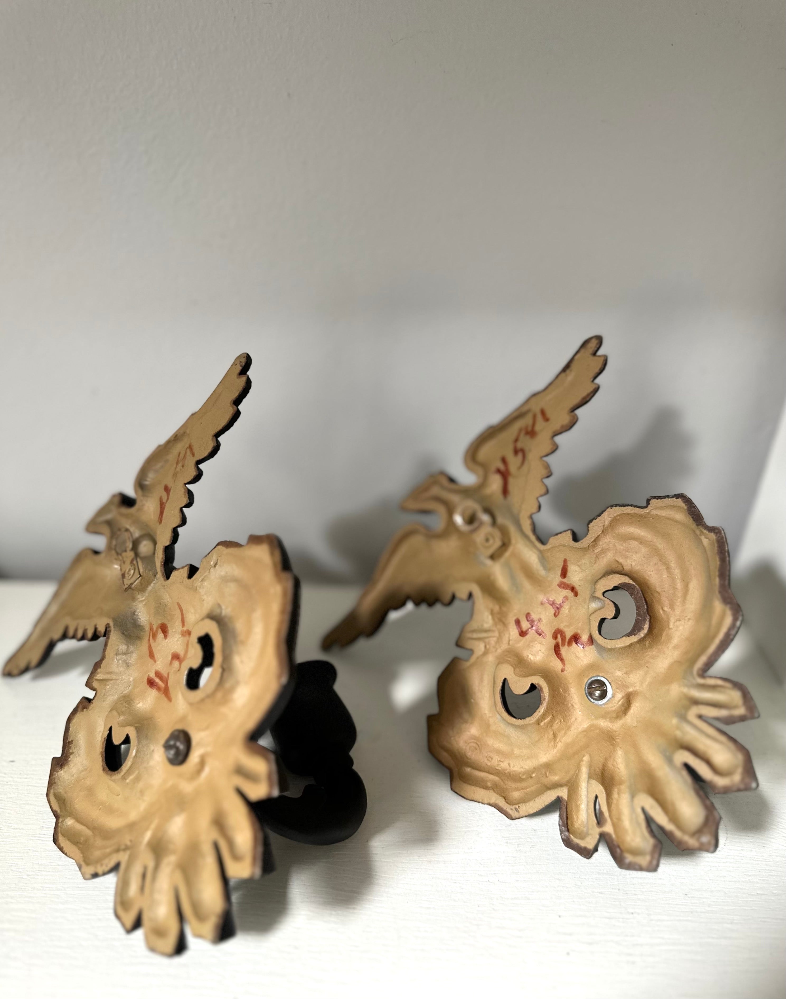 A pair of vintage-style wooden bird-shaped ornaments or decorative pieces with carved facial features and small red painted markings, displayed against a plain light background.