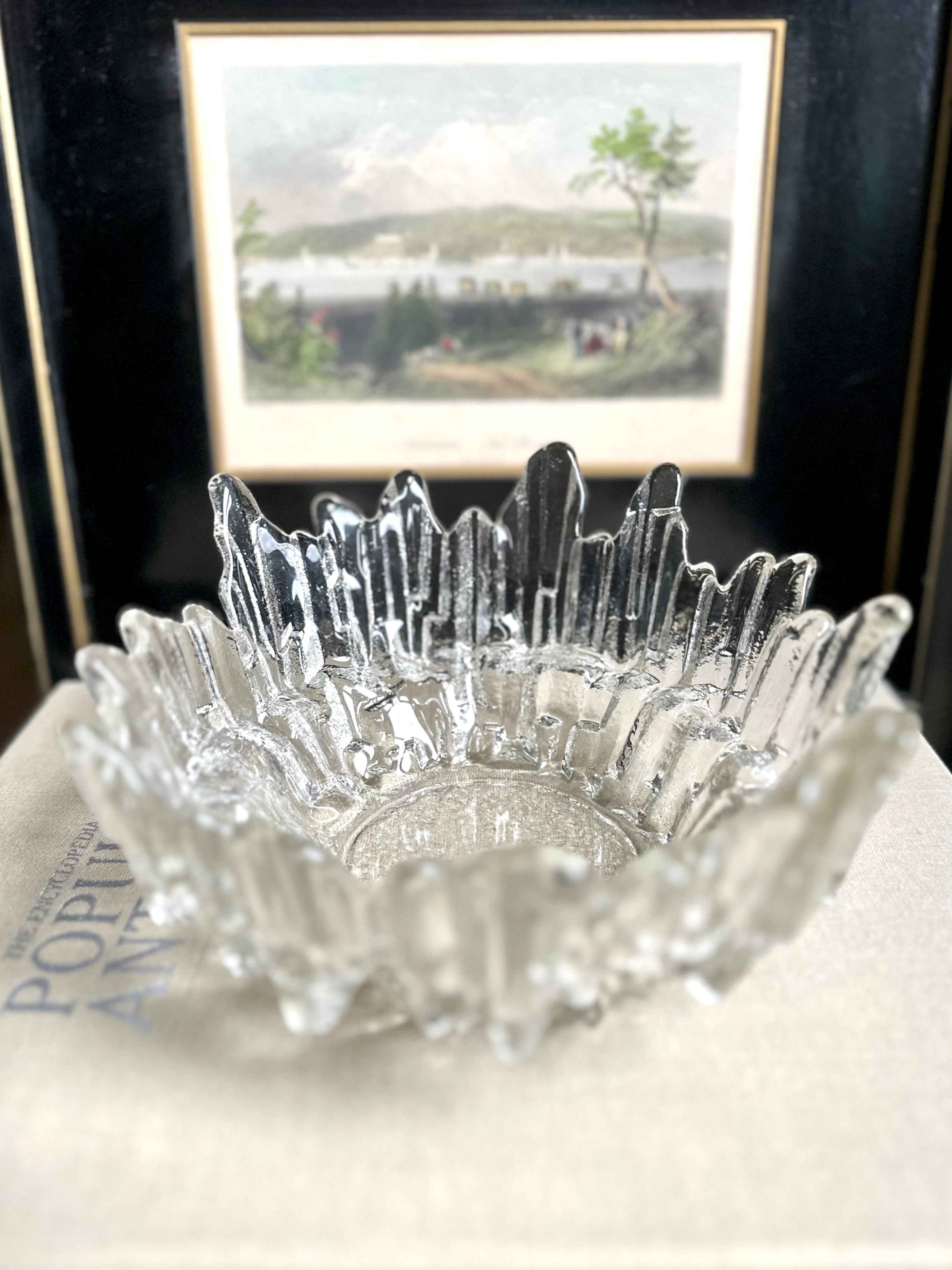 Vintage textured glass bowl sitting on a book about antiques, a black and white framed print in the background