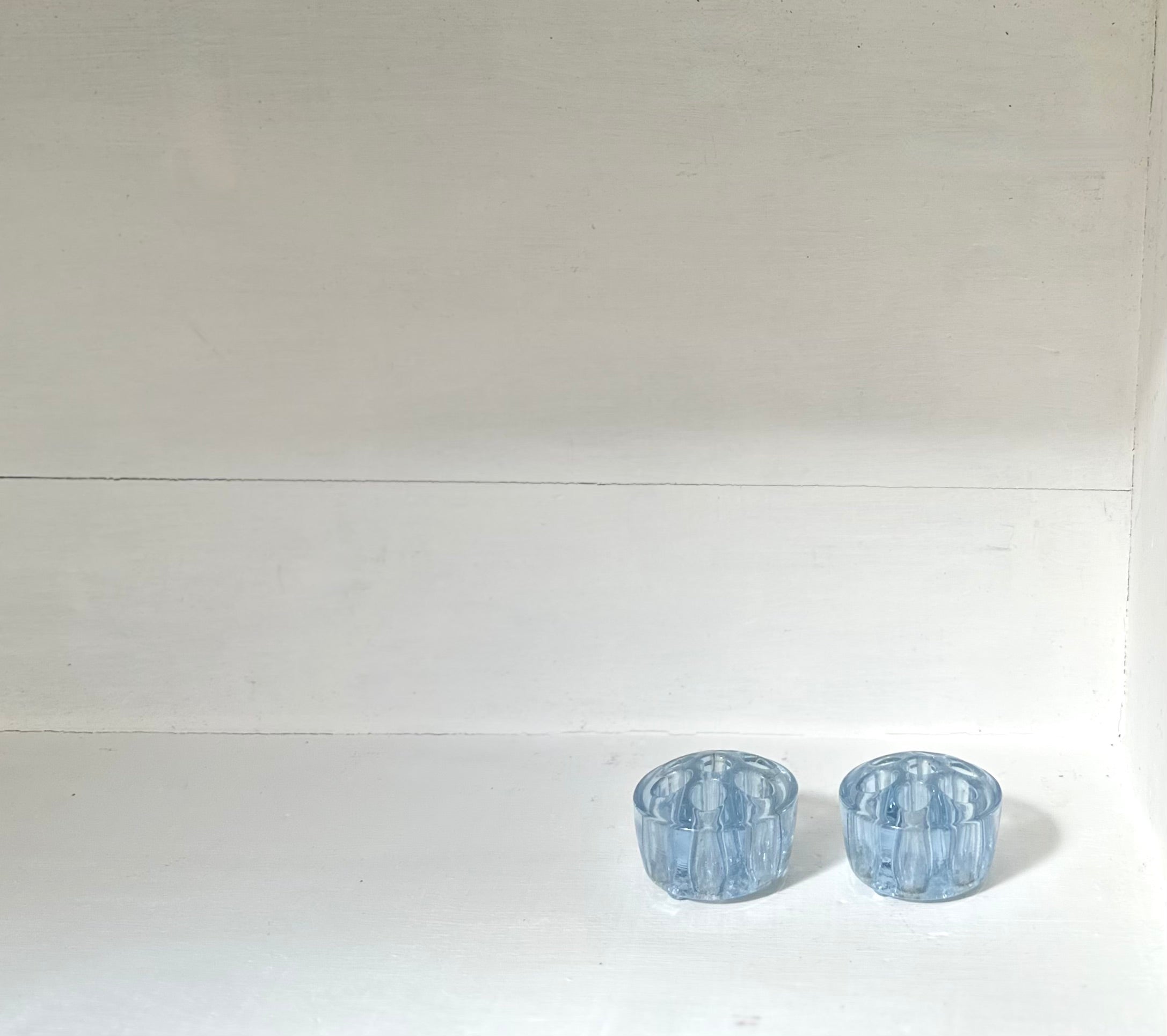 Two small light blue faceted glass cups or candle holders placed side by side on a white surface against a white background.