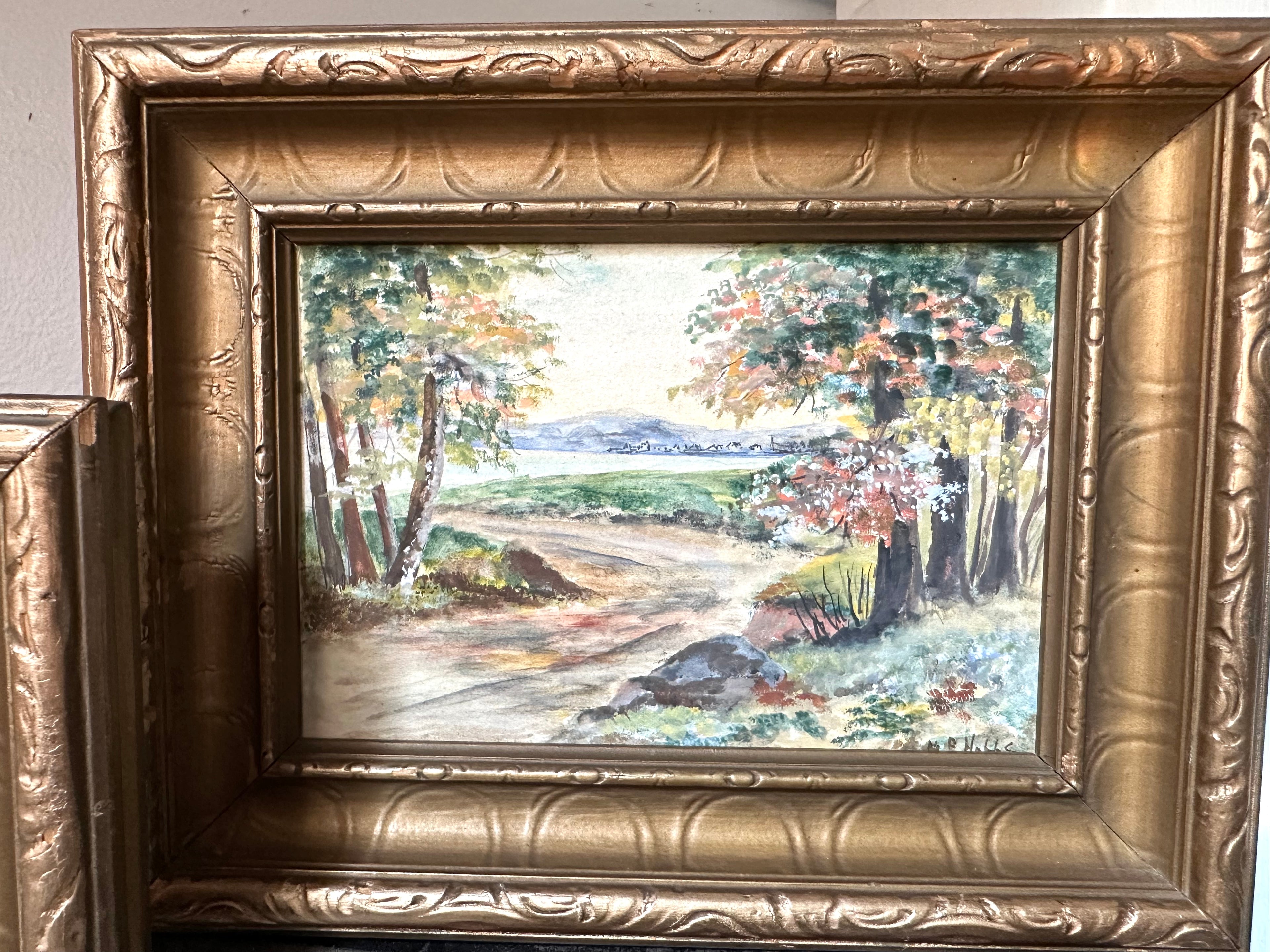 A framed landscape painting showing a dirt road winding through trees with green, yellow, and brown foliage, set in an ornate gold frame.