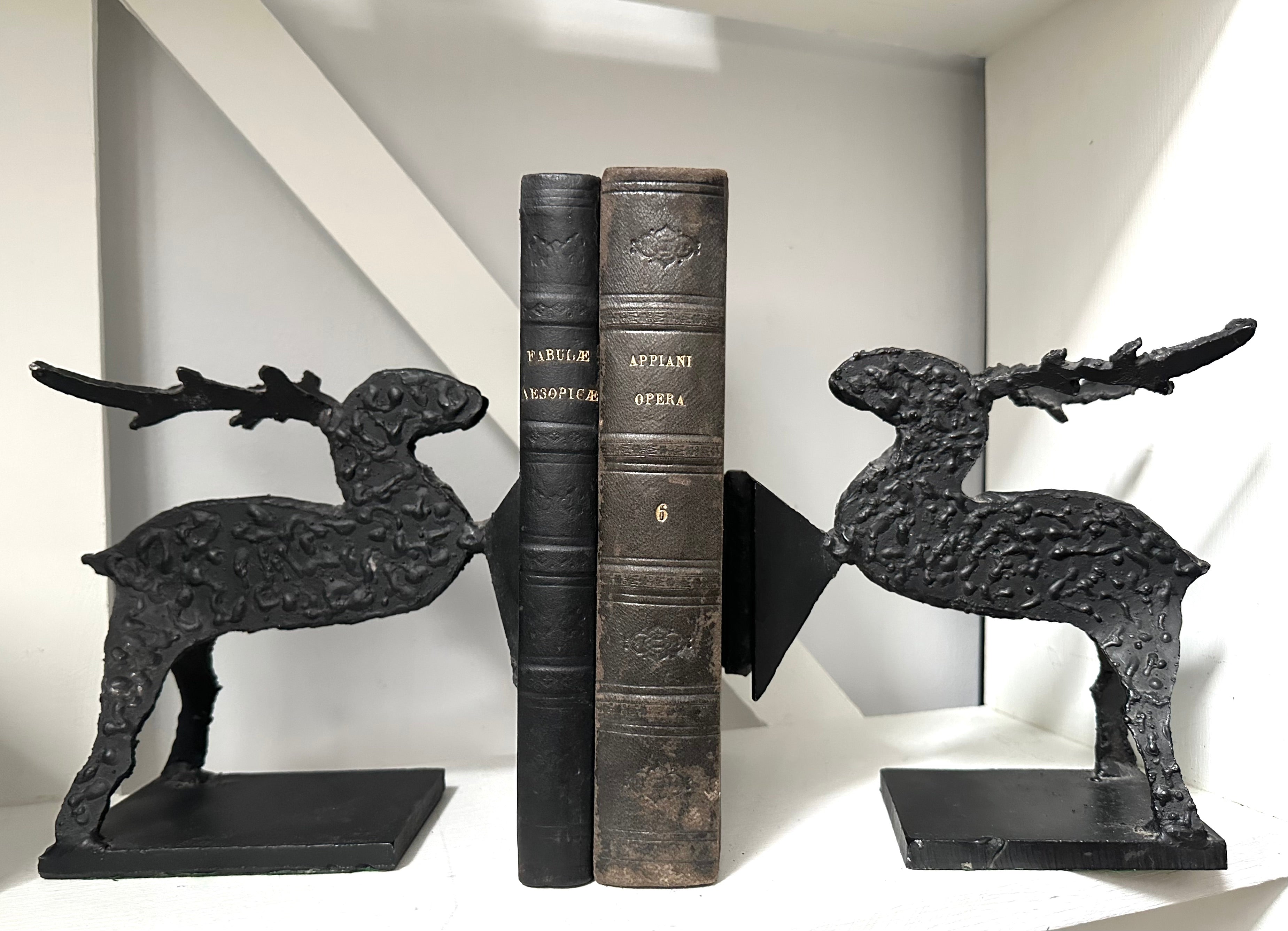 Decorative black deer bookends holding books against a white wall.