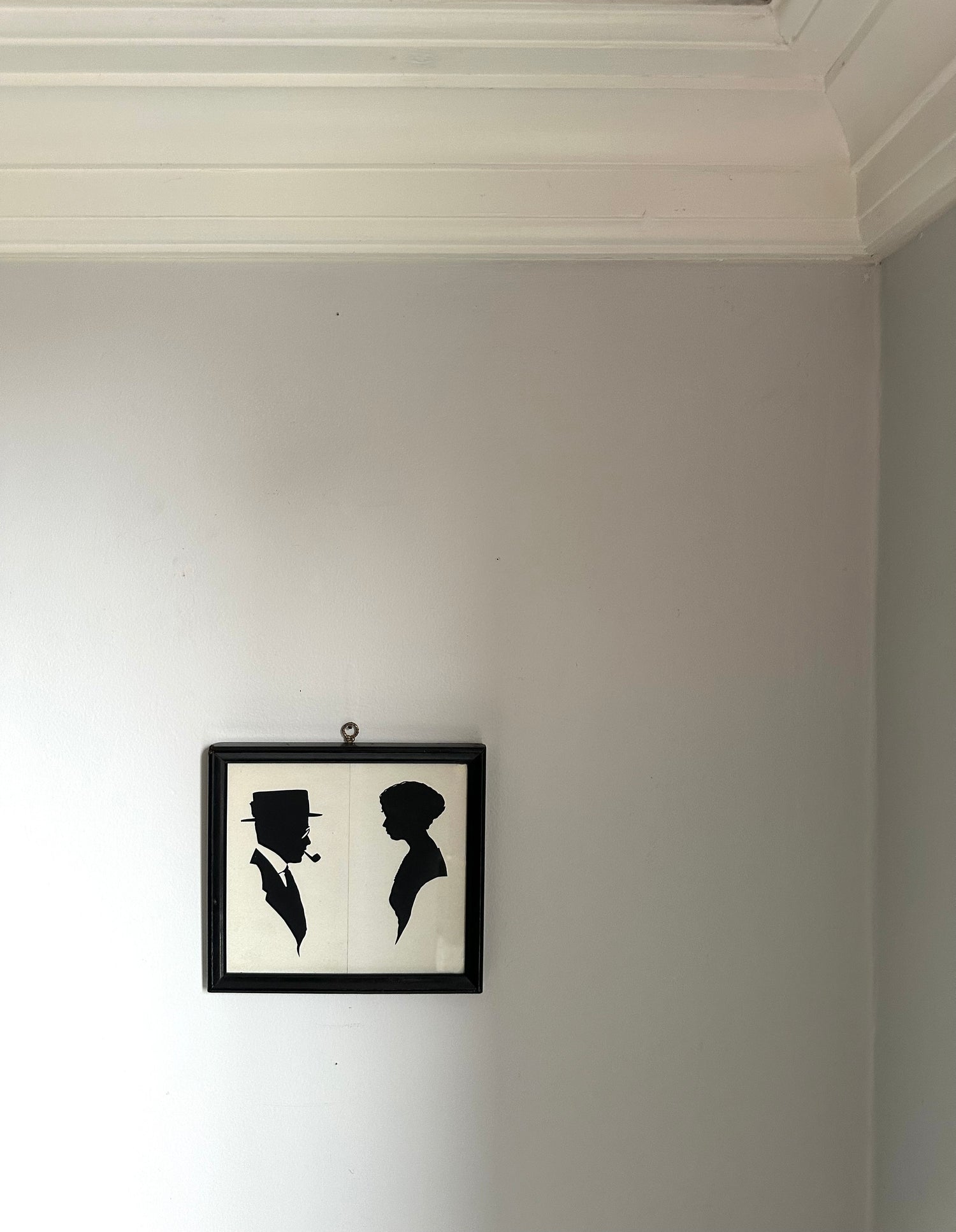 A small black-framed wall art piece hanging on a light gray wall, featuring black silhouette portraits of a man and a woman on a white background.