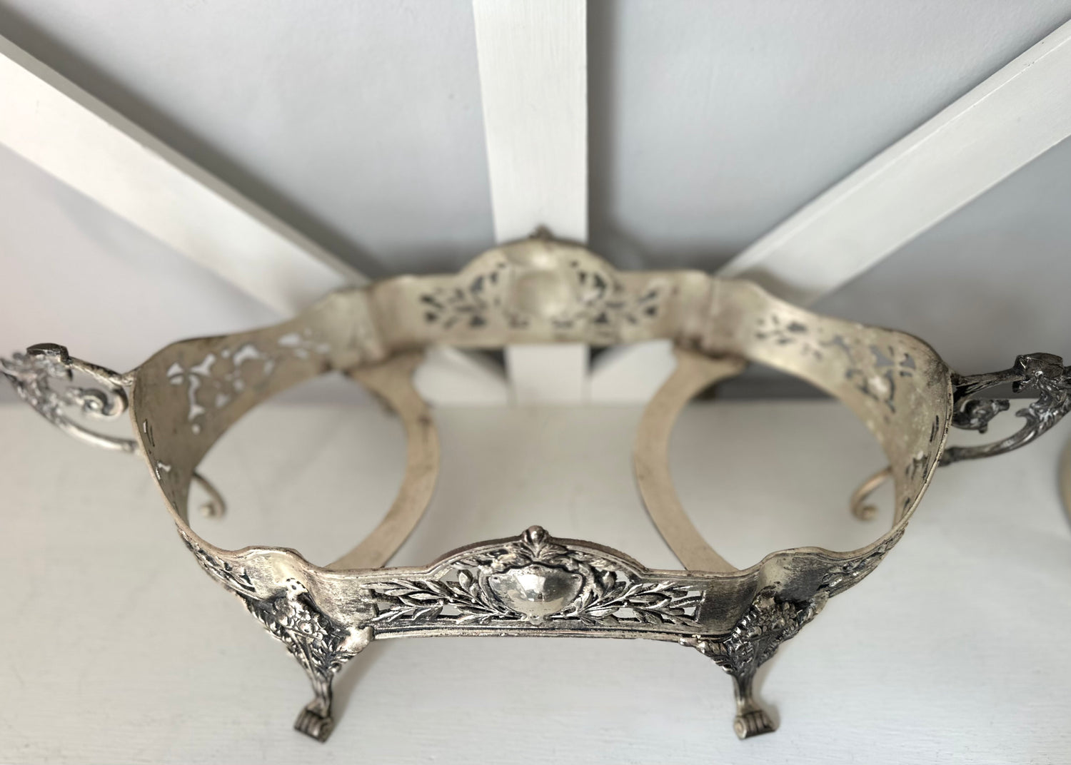 An ornate silver metal stand with decorative filigree cutouts, scrollwork, and small feet, photographed against a white background.