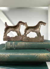 Two metal dog-shaped bookends on top of a green book with gold text.