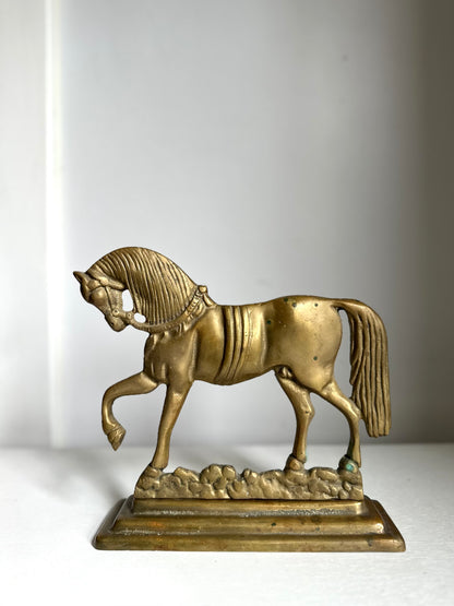 A small metallic horse figurine on a rectangular base, photographed against a plain light gray background.