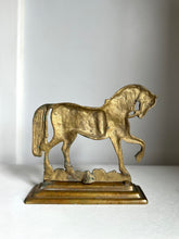 An antique-style metallic horse figurine standing on a rectangular base, photographed against a plain light gray background.