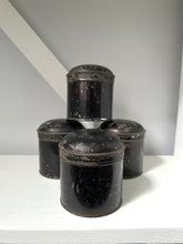 Set of four black metal canisters on a white surface with a gray background