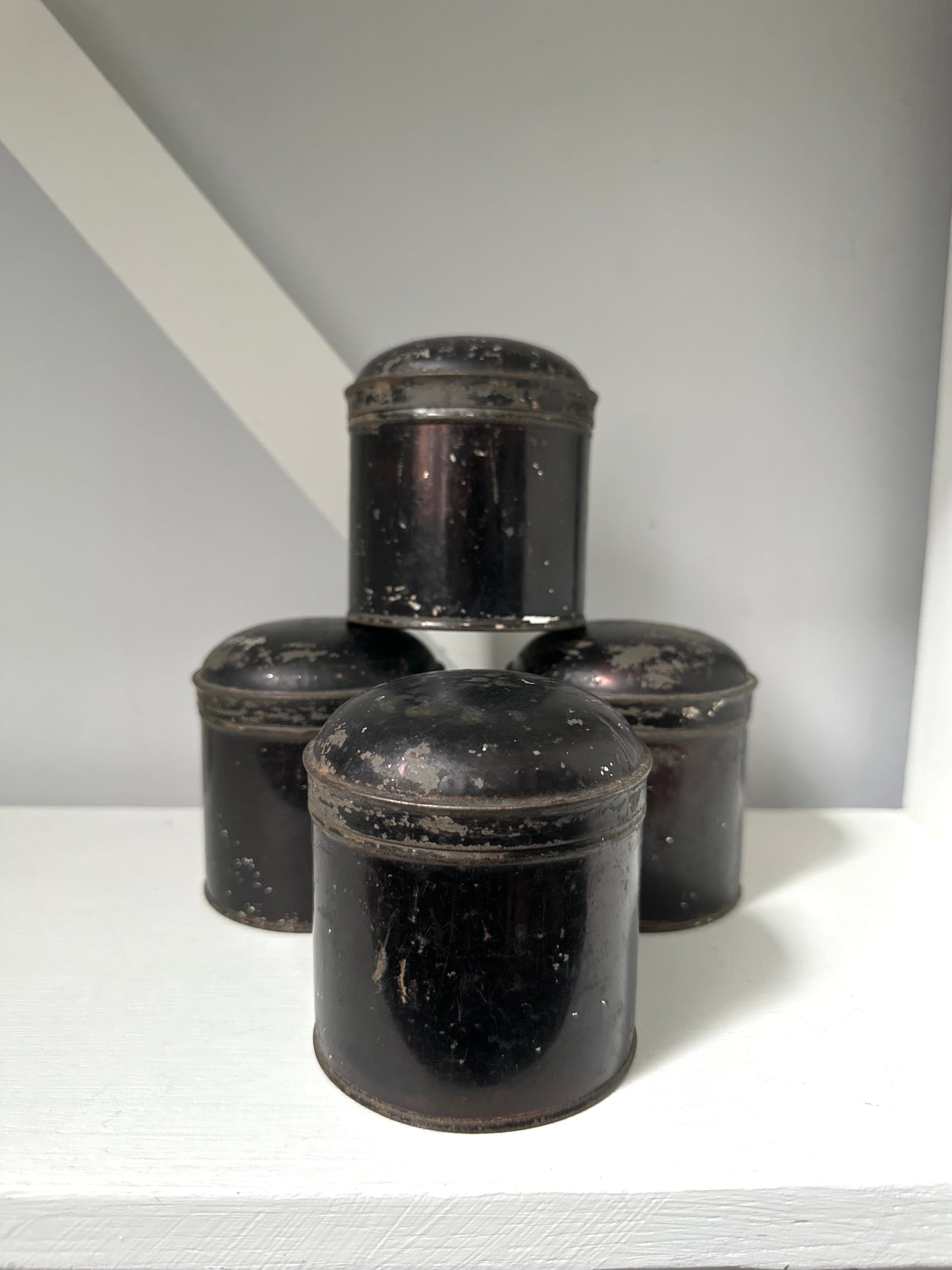 Set of four black metal canisters on a white surface with a gray background