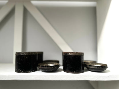 Black cylindrical objects on a white shelf with a white wall background