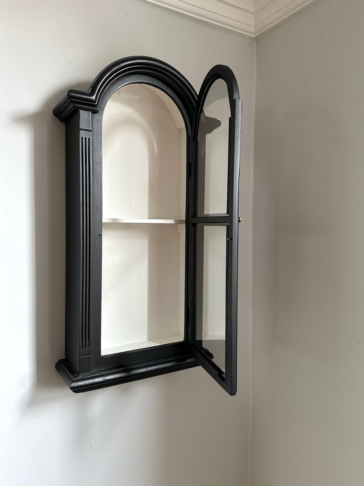 Black-framed antique display cabinet leaning against a light gray wall 