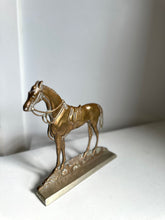 A small metallic horse figurine standing on a rectangular base, photographed against a plain light gray background.