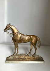 A metallic horse figurine sculpture in a bronze finish, standing on a textured base with a polished rectangular pedestal, photographed against a neutral light gray background.
