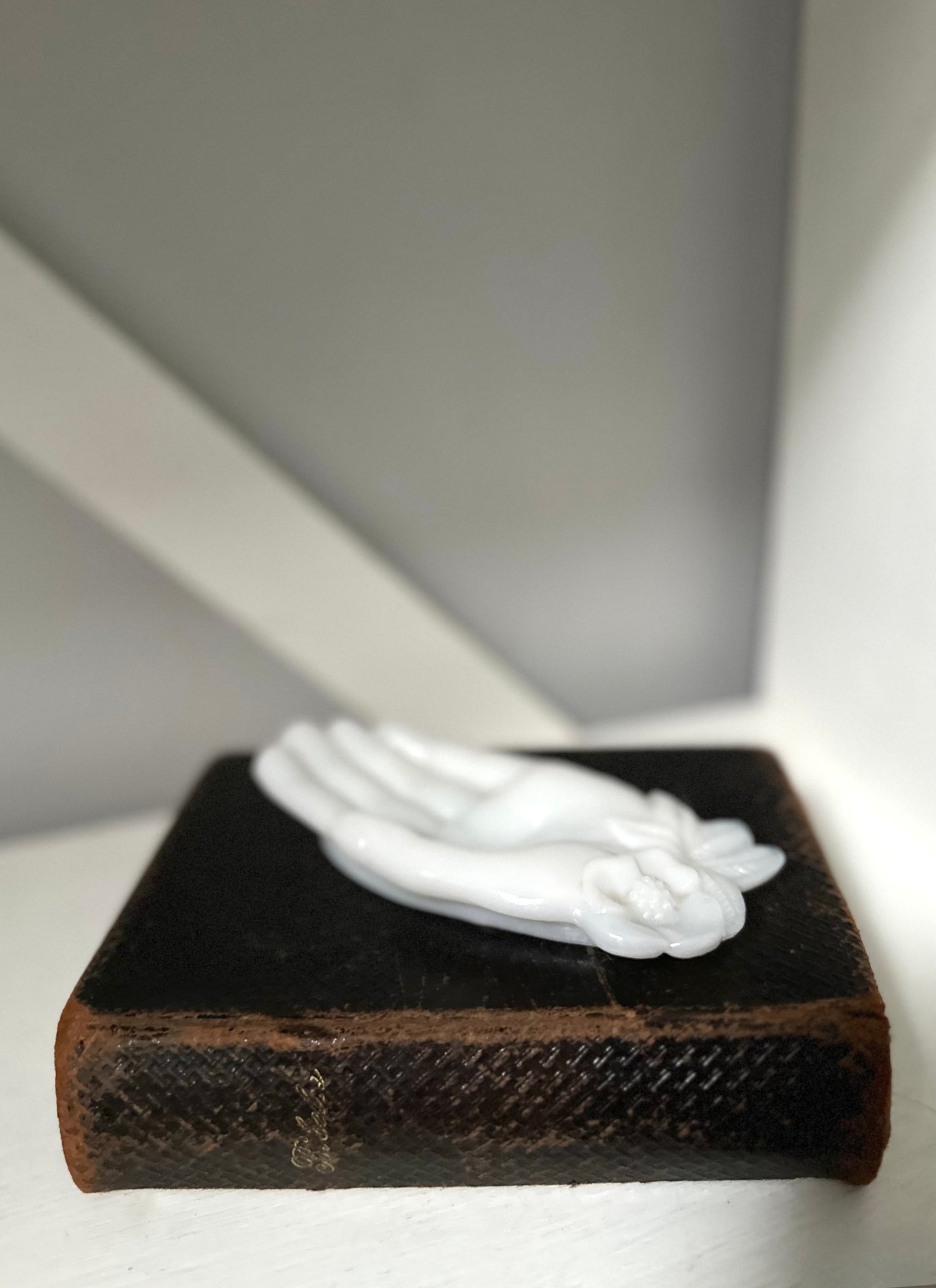 Small white sculpture on a dark brown base against a neutral background