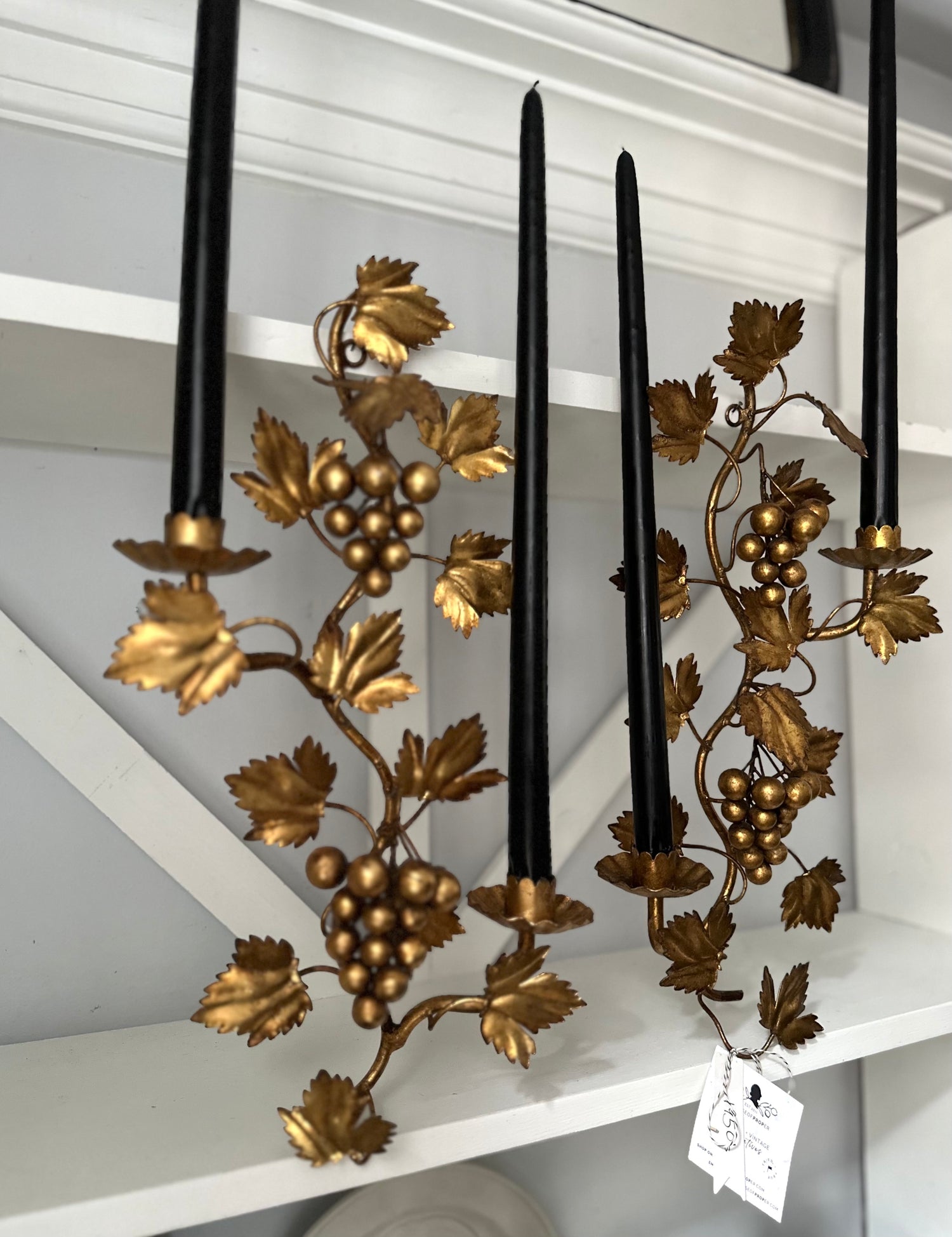 Decorative candle holder with gold leaf and grape design on a white shelf.