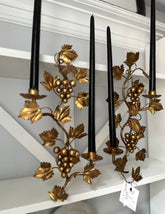 Decorative candle holder with gold leaf and grape design on a white shelf.