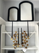 Decorative wall sconces with black frames and gold leaf design on a white shelf.