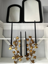 Decorative wall sconces with gold leaf design on a white shelf.