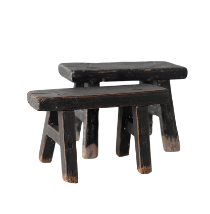 Two wooden stools with a worn black finish on a white background