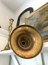 Close-up of a brass candle holder on a shelf with a painting in the background