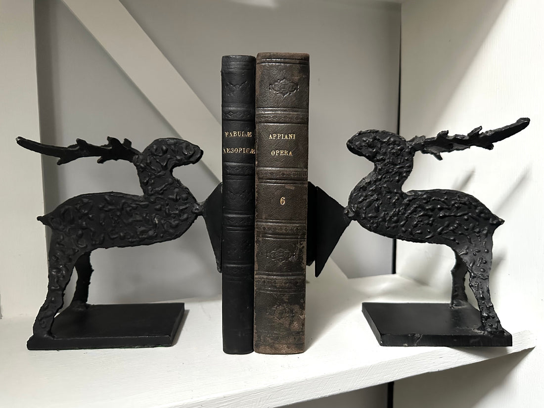 Black cast iron deer bookends holding open a vintage book on a white shelf.
