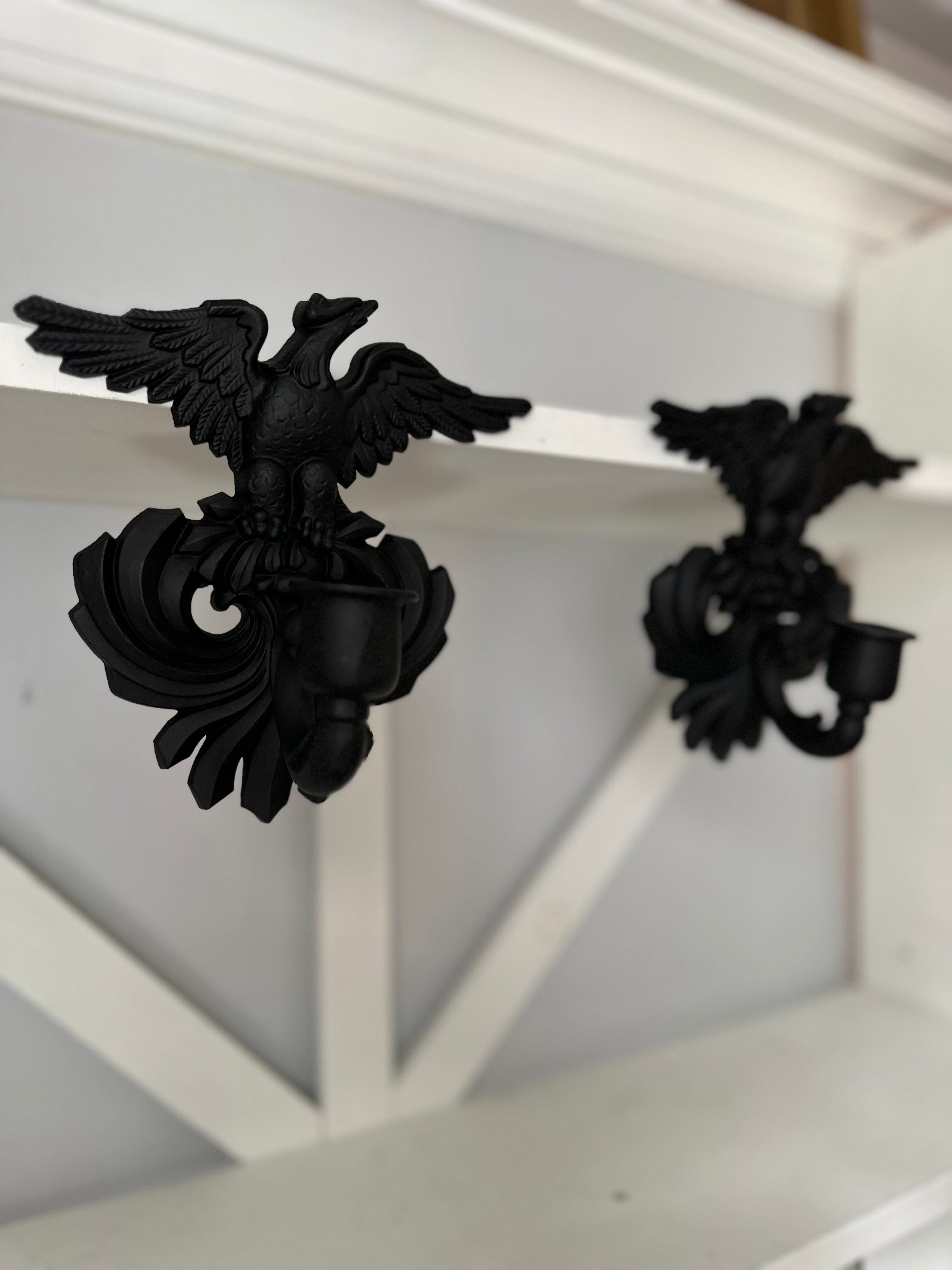 A pair of black cast iron eagle wall sconces mounted on a white wooden mantel shelf.