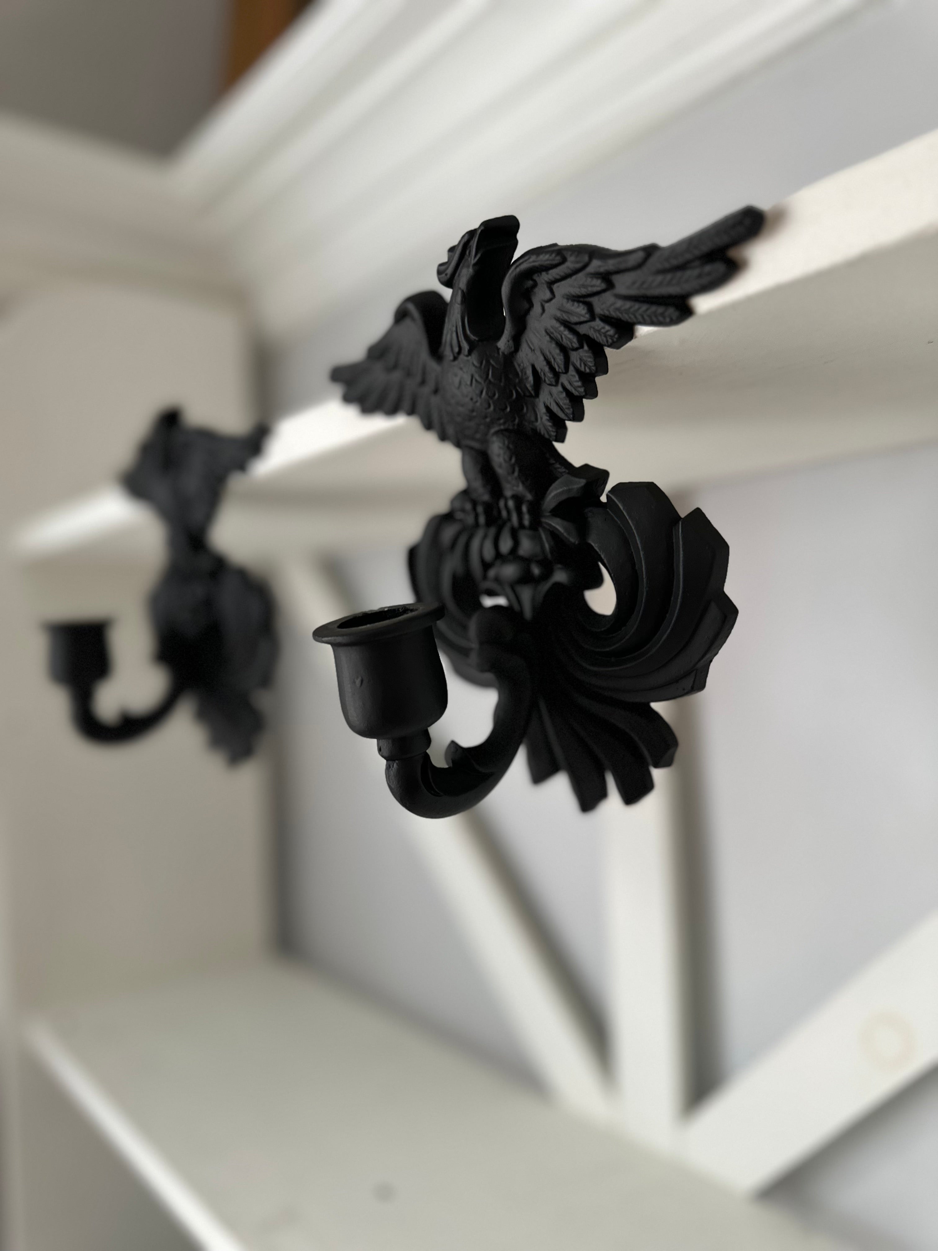 Black metal wall sconces shaped like winged griffin figures mounted on a white wooden shelf.