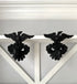 A pair of black metal eagle wall hooks mounted on a white wooden shelf against a light gray wall.
