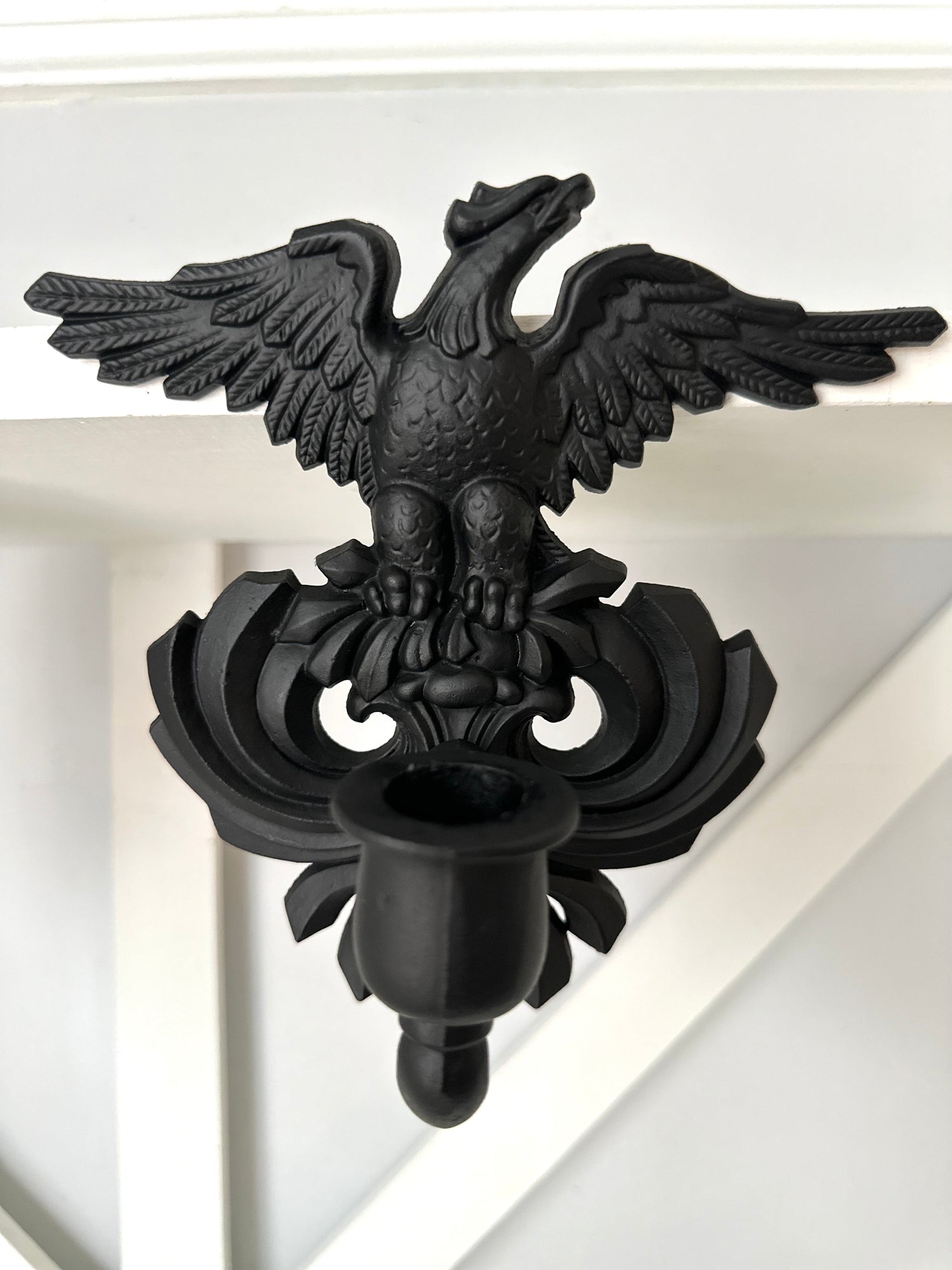 A black metal double eagle wall sconce mounted on a white painted wooden wall or shelf.